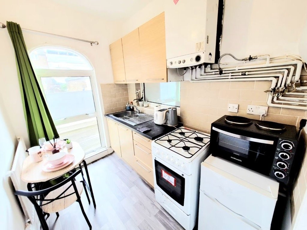 A compact UK rental kitchen with a small fridge, gas cooker, kettle and wall-mounted boiler