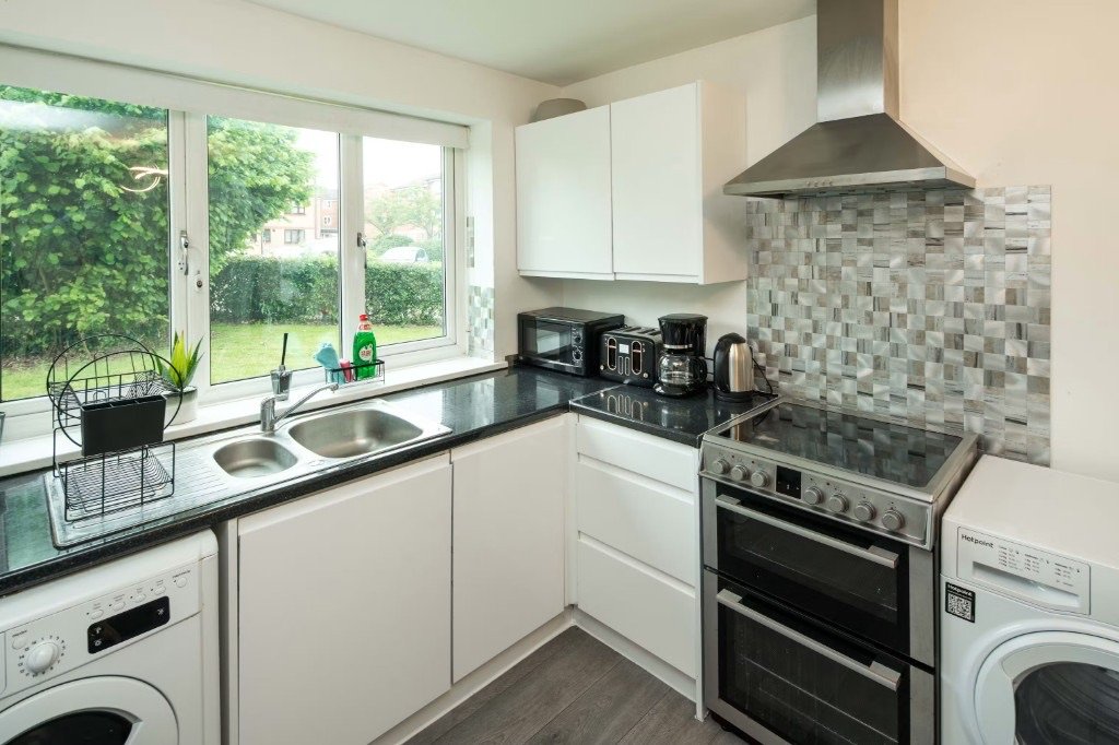 A fitted UK kitchen with a dishwasher under the sink, a washing machine, hob and oven